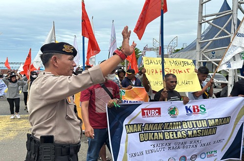 Seorang polisi mengamankan aksi unjuk rasa Serikat Buruh Sawit di Kotabaru, Kalimantan Selatan, dengan peserta membawa spanduk tuntutan.