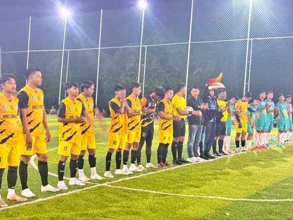 Para pemain sepak bola mengenakan seragam kuning dan hijau berbaris di lapangan Mini Soccer Bamega Kotabaru pada malam hari, disinari lampu sorot, menjelang penutupan turnamen Bamega Cup 2025.