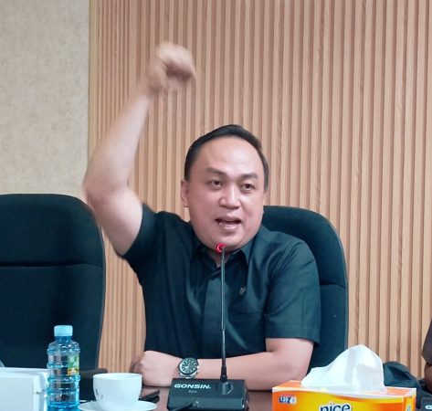 dr. Muhammad Yadi Mahendra Muhyin mengenakan kemeja hitam, berbicara tegas dengan tangan terangkat dalam sebuah rapat